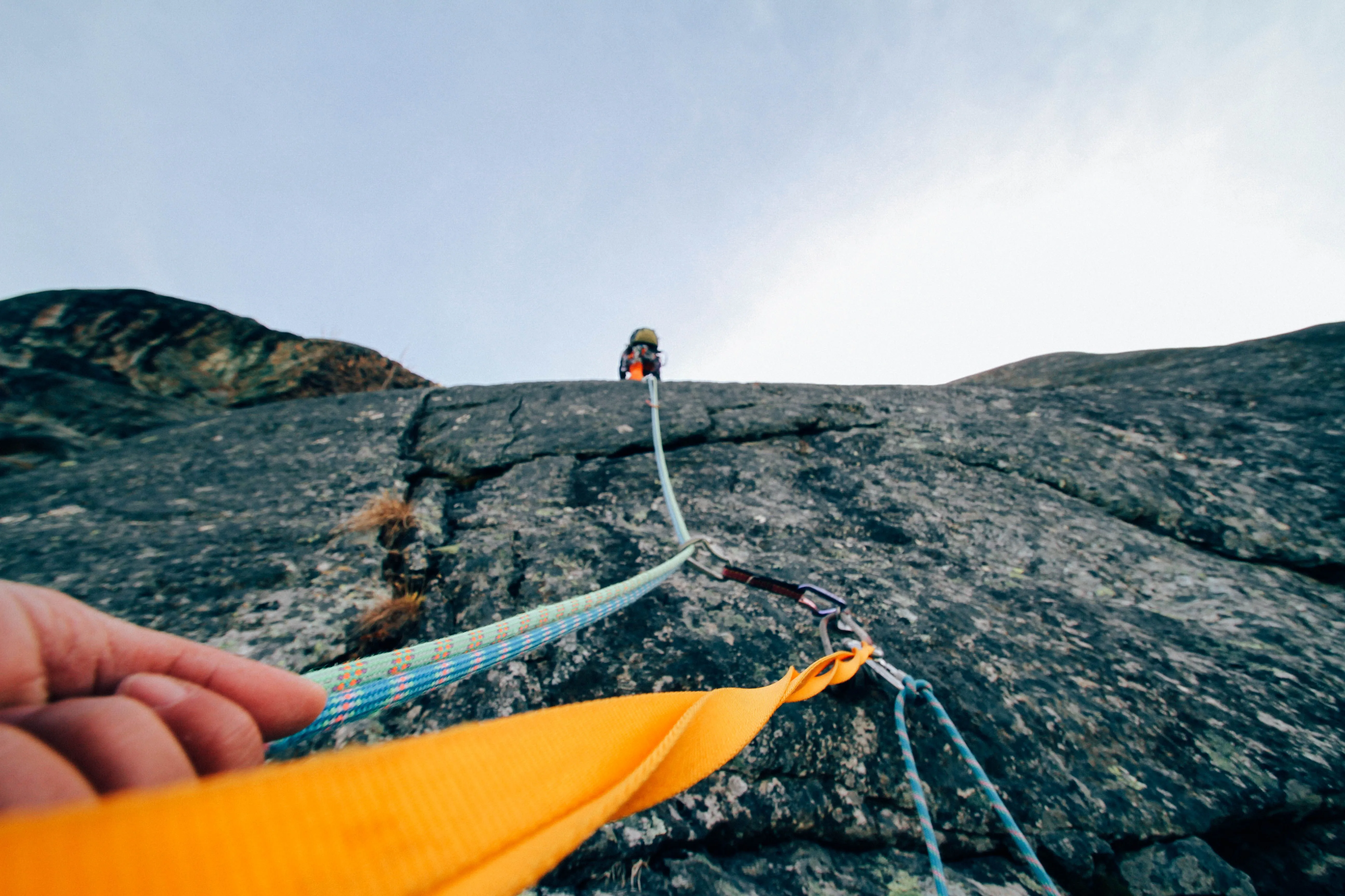 View from a rock climber looking up a cliff face, following a rope through protection anchors set by a lead climber above